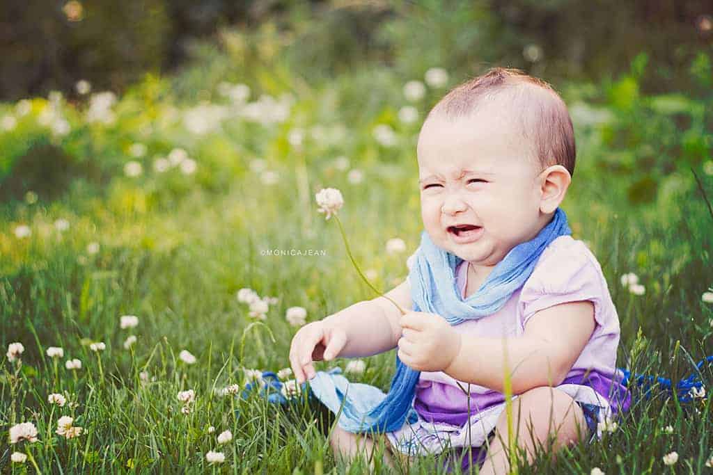 Infant crying on grass holding a flower