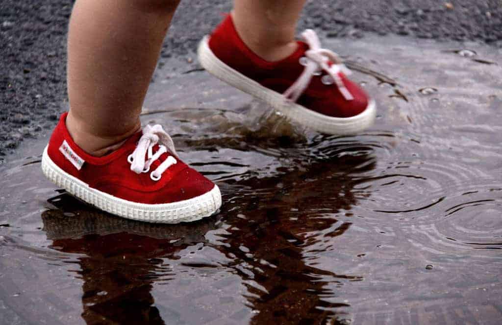 Toddler walking through puddle wearing little red shoes