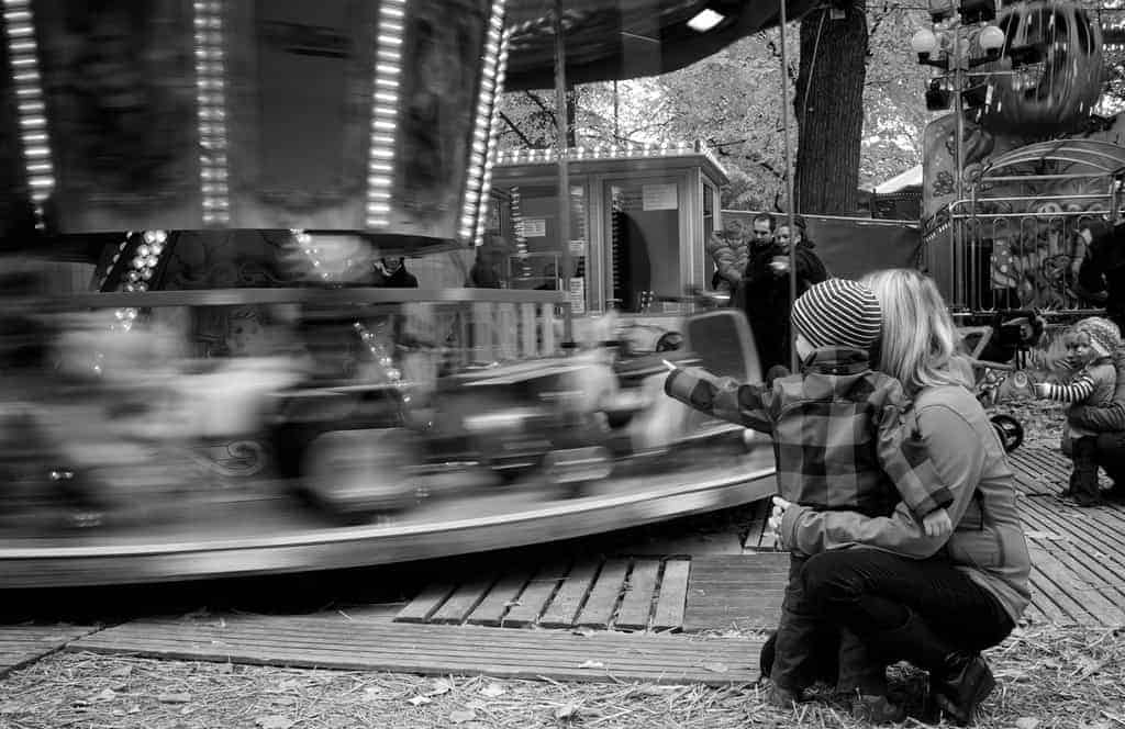 Mother and toddler looking at merry go round spinning b&w
