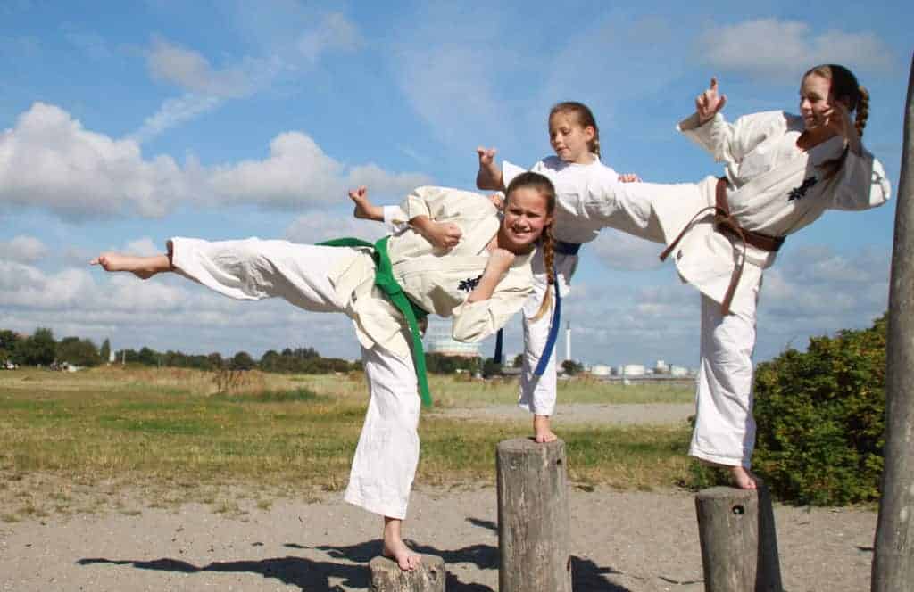 Three girls doing karate kicks on posts outside