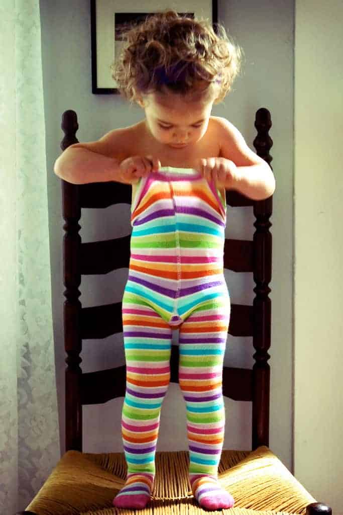 Two year old toddler putting on rainbow tights all by herself.