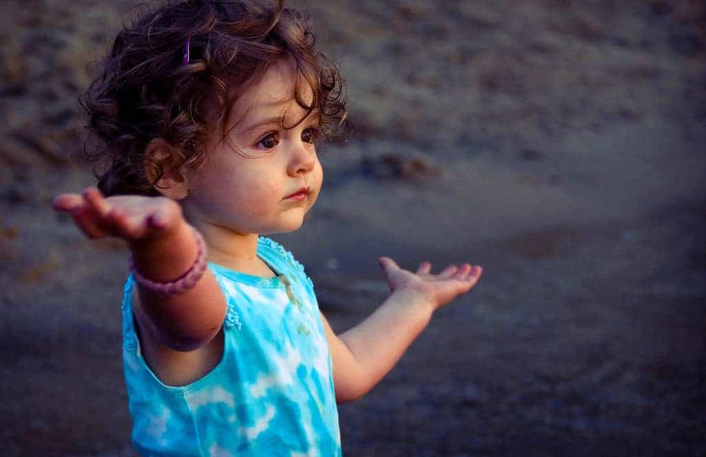 Two year old toddler at beach raising her hands in wonder