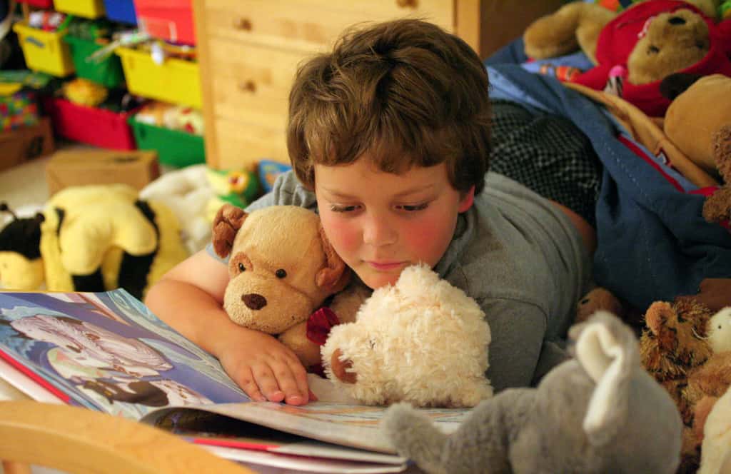 Preschooler reading on bed with stuffed animals