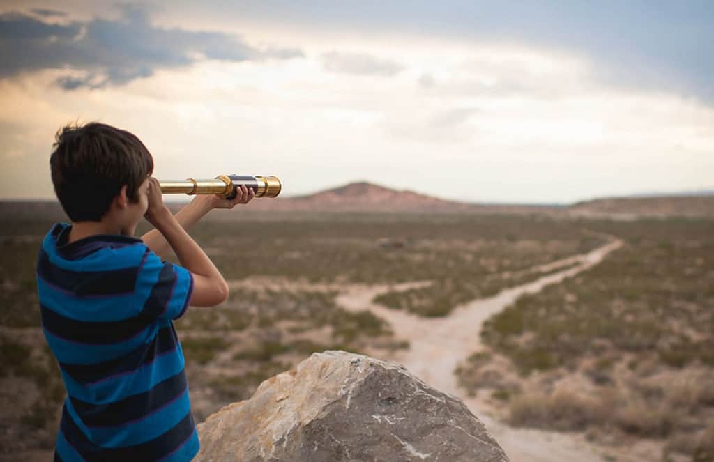 Boy looking through telescope in desert