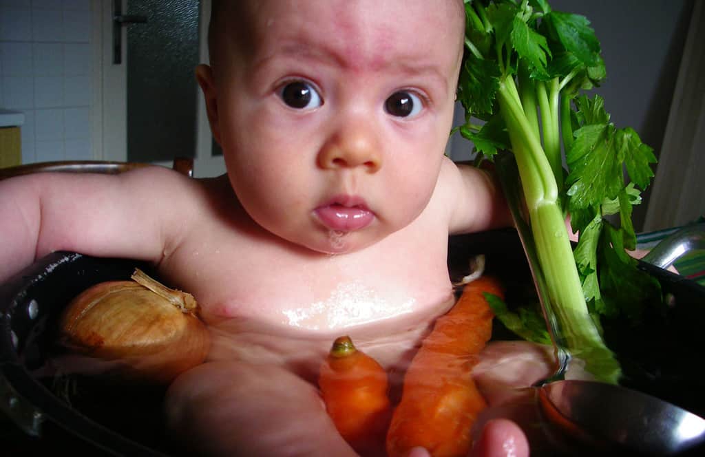 Baby sitting in pot with water and vegetables