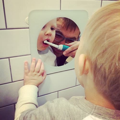 Father using electric toothbrush on toddler teeth